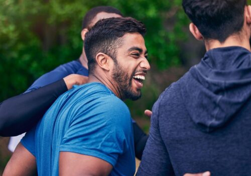 Young Indian man laughing with friends during exercise session in a park