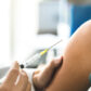 Close-up of arm of young adult woman with rolled up sleeve and hands of healthcare professional preparing to administer vaccine injection to illustrate part of public health response to meningitis B outbreak