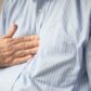 Close up of mid-section of middle aged male business man putting hand to mid-chest to indicate discomfort from heart burn and illustrate use of proton pump inhibitor (PPI)