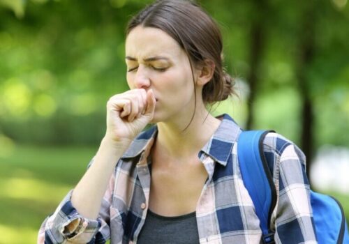 Woman clearing her throat/coughing outside by some trees