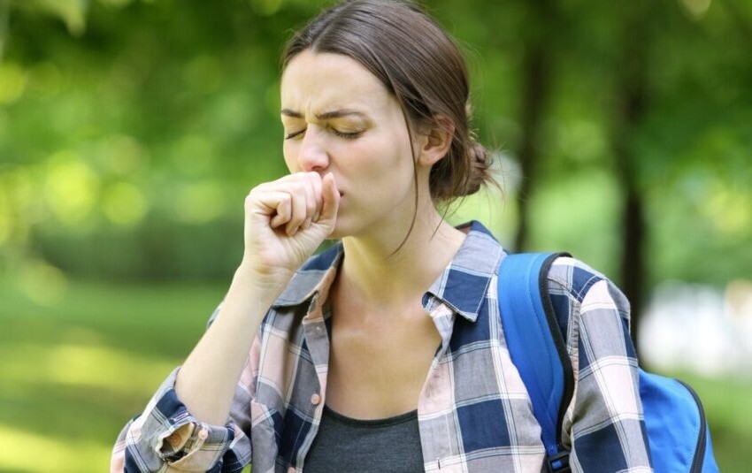 Woman clearing her throat/coughing outside by some trees