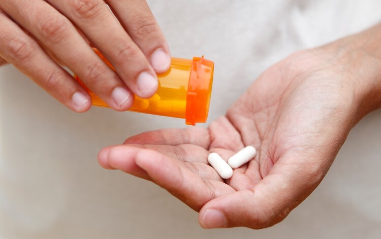 Person tipping some white pills into their palm
