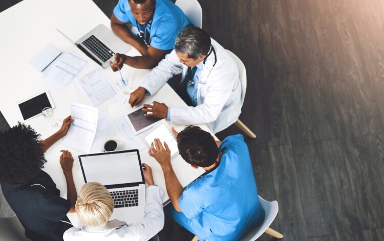 Healthcare professionals sit around a table with laptops and paper