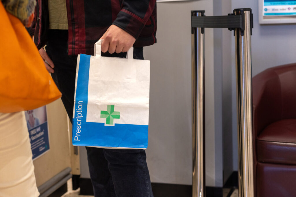 A medium shot of an unrecognisable person holding a bag of prescription medication he has just collected from the pharmacy.