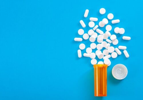 Medicine, opioid painkillers and prescription medicines concept with top view of orange prescription bottle of oxycodone and hydrocodone pills spilled on a blue background with copy space