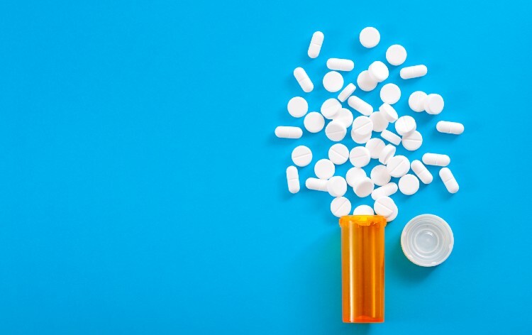 Medicine, opioid painkillers and prescription medicines concept with top view of orange prescription bottle of oxycodone and hydrocodone pills spilled on a blue background with copy space