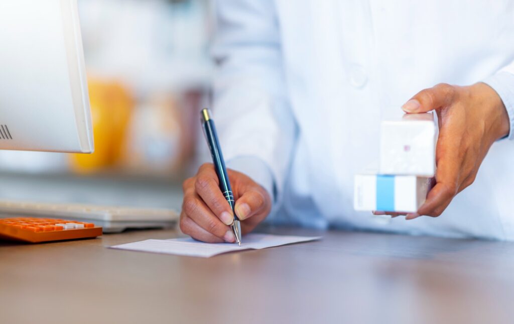 pharmacist writing a prescription while holding medicines
