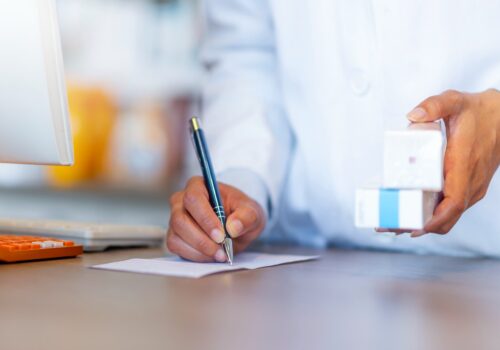 pharmacist writing a prescription while holding medicines
