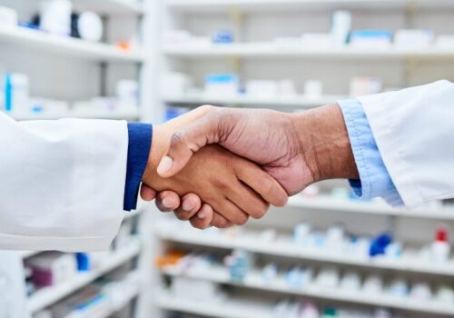 A pharmacist and doctor shake hands in a pharmacy