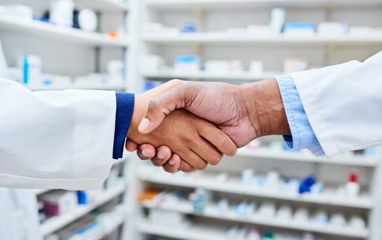 A pharmacist and doctor shake hands in a pharmacy