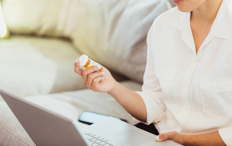 Woman holding a bottle of medicine and looking at a computer