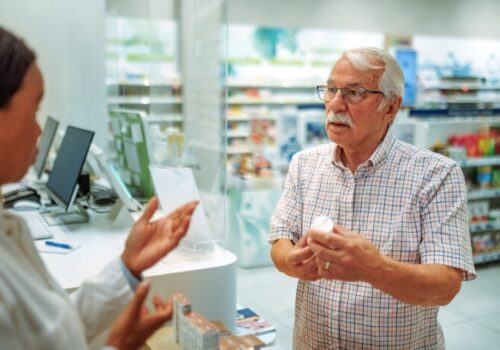 Old man looking annoyed while talking to a pharmacist