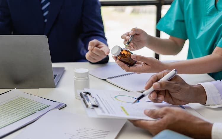 A team of medical professionals sitting around a table. One doctor is holding a jar of pills