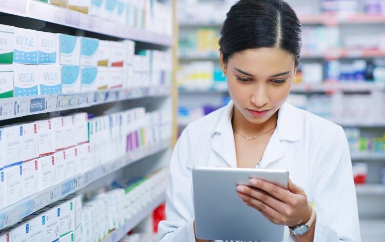 Pharmacist-looking-at-computer-tablet-while-surrounded-by-boxes-of-medicines