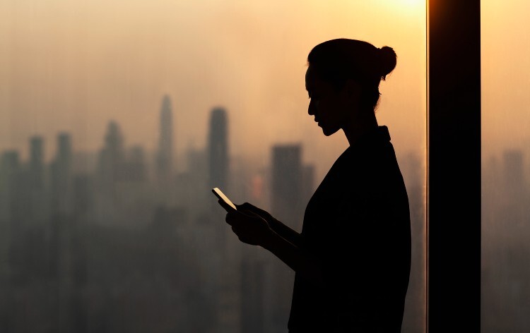 Woman looks at an app on her phone with a city skyline in the background