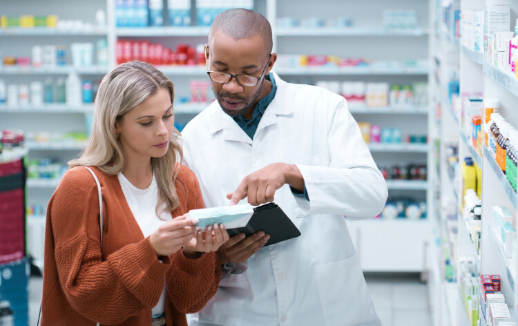 A pharmacist wearing a white coat and speaking with a patient.