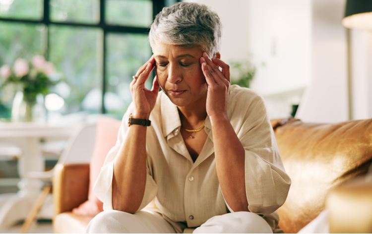 Headache, stress and senior woman on sofa in home with fatigue, tension or brain fog in living room.