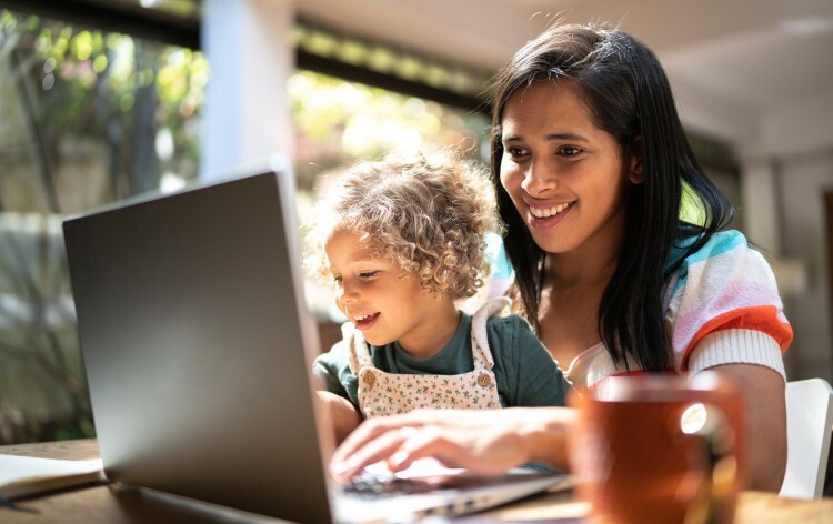Mother using a laptop while holding her daughter at home