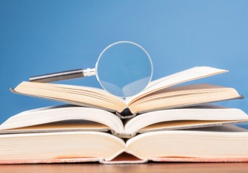 Open book with magnifying glass on wooden desk in information library of school or university, concept for education,reading , study, copy space and blue background.