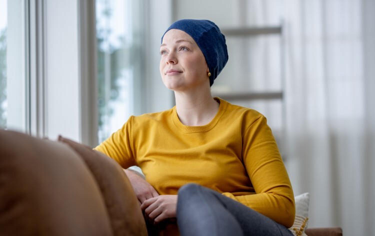 A young woman battling Cancer sits on the sofa in her home