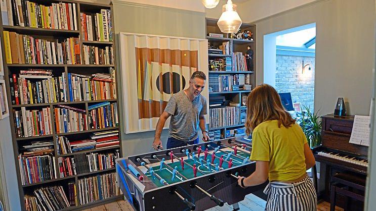 Face-off: Remi and Michelle play table football in front of a library of art books; and (below) their stylish wood-burning stove