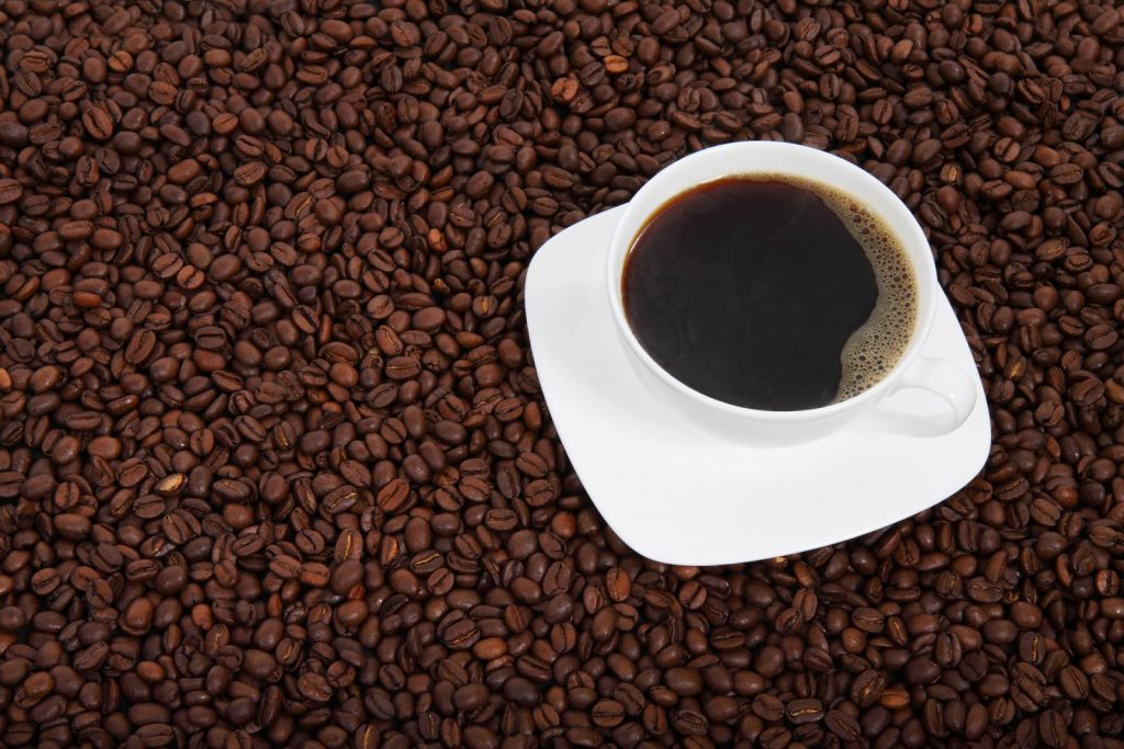cup of coffee sat on a bed of coffee beans - choosing a good coffee grinder