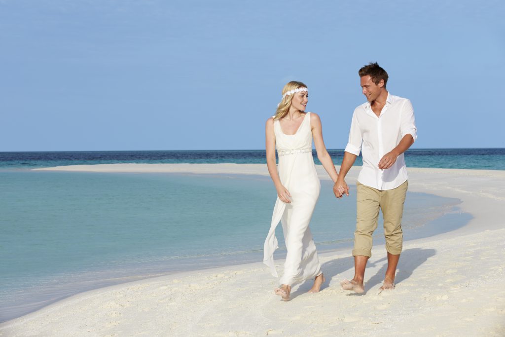 bride and groom, barefoot on the beach. tips for choosing your wedding shoes