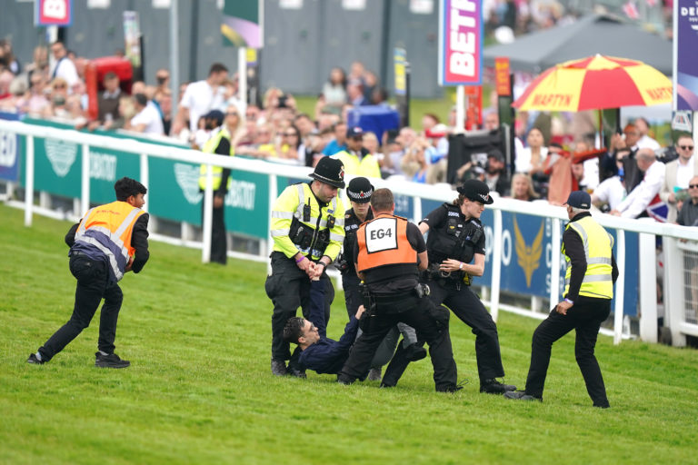 A protestor is escorted off the track by police and stewards during the Derby
