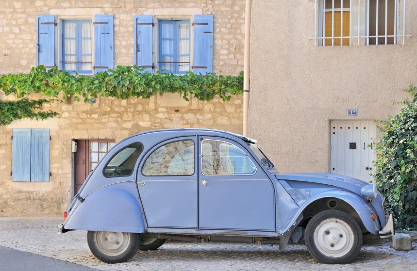 Classic french provincial village scene featuring blue citroen car and old buildings with shutters