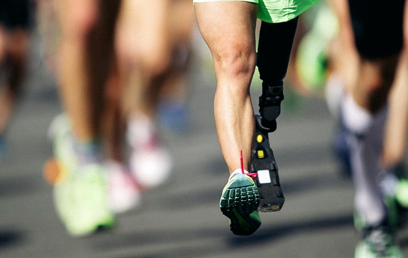 People running in a race. The person in focus has a prosthetic leg.