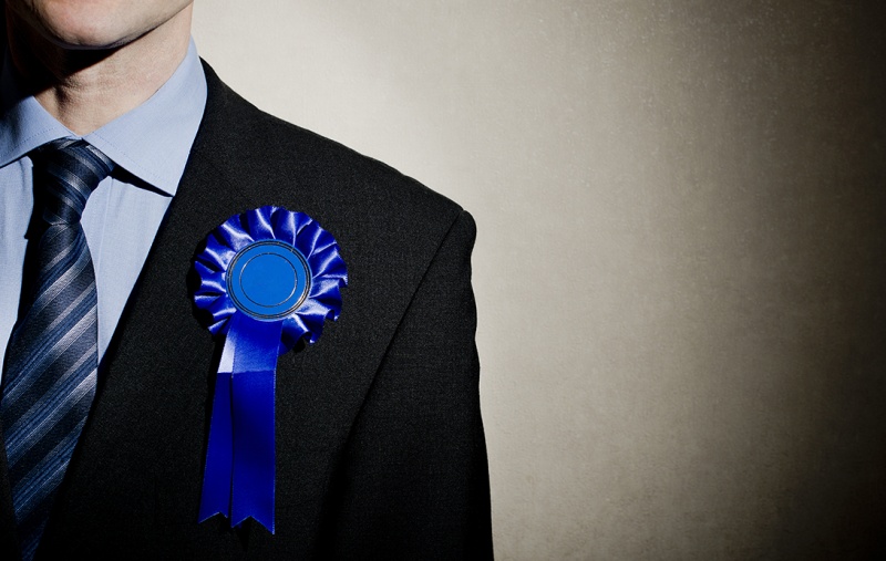 A man in a suit wearing a blue rosette