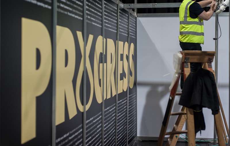 Sign reading "Progress" at SNP Conference while a construction worker fits a frame together on a ladder