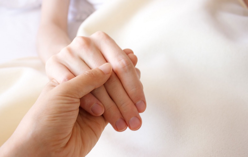 A person holding the hand of a bed-bound person