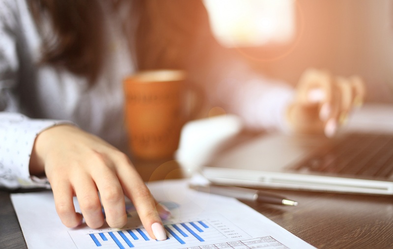 A woman sitting at a laptop with one hand on a sheet of paper containing a graph