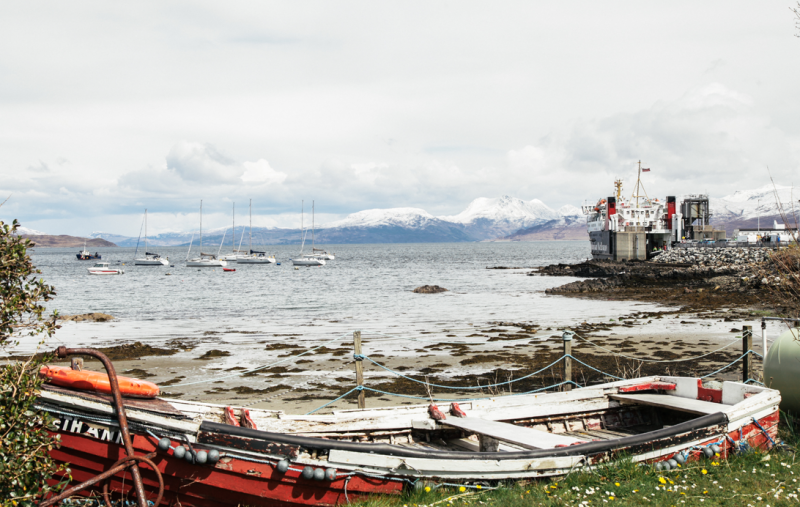 A rowing boat by the seashore - a CalMac ferry is in the distance