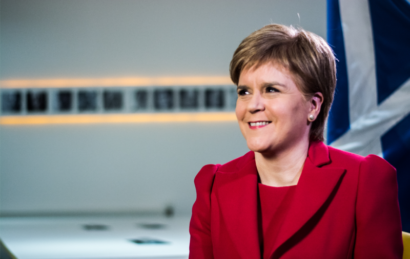 Nicola Sturgeon sitting in SNP HQ with a saltire in the background