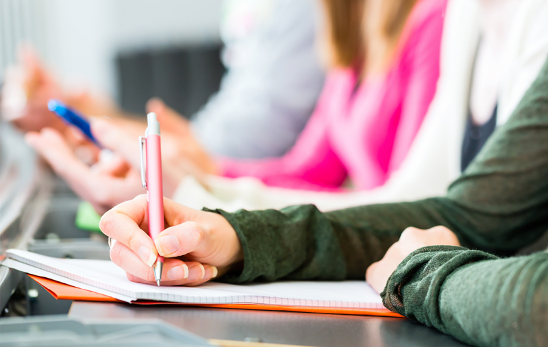 Young person writing onto a pad of paper in a classroom