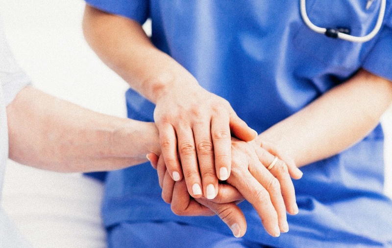 Close up of a nurse touching hand of a patient in hospital ward
