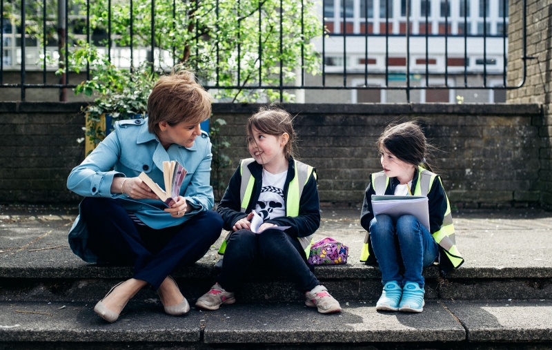 Nicola Sturgeon holding a book sitting down talking to two wee girls