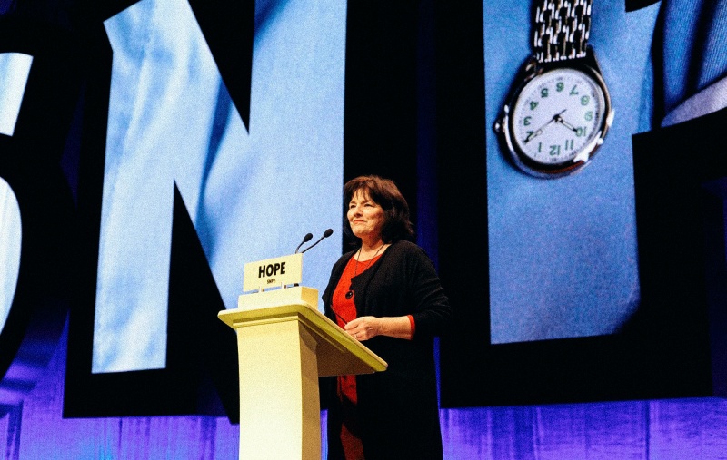 Jeane Freeman speaking at Conference in front of a picture of a nurse