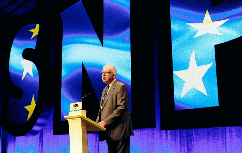 Michael Russell speaking at Conference in front of the EU flag within the SNP letters