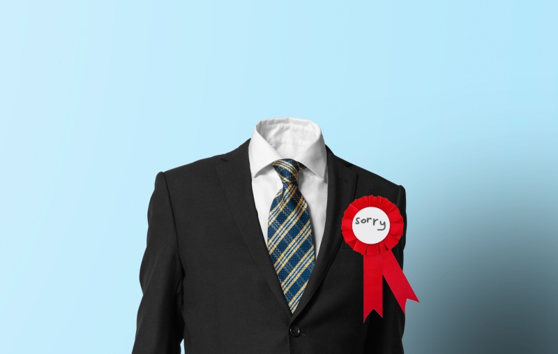 an empty suit wearing a red rosette that reads "sorry"